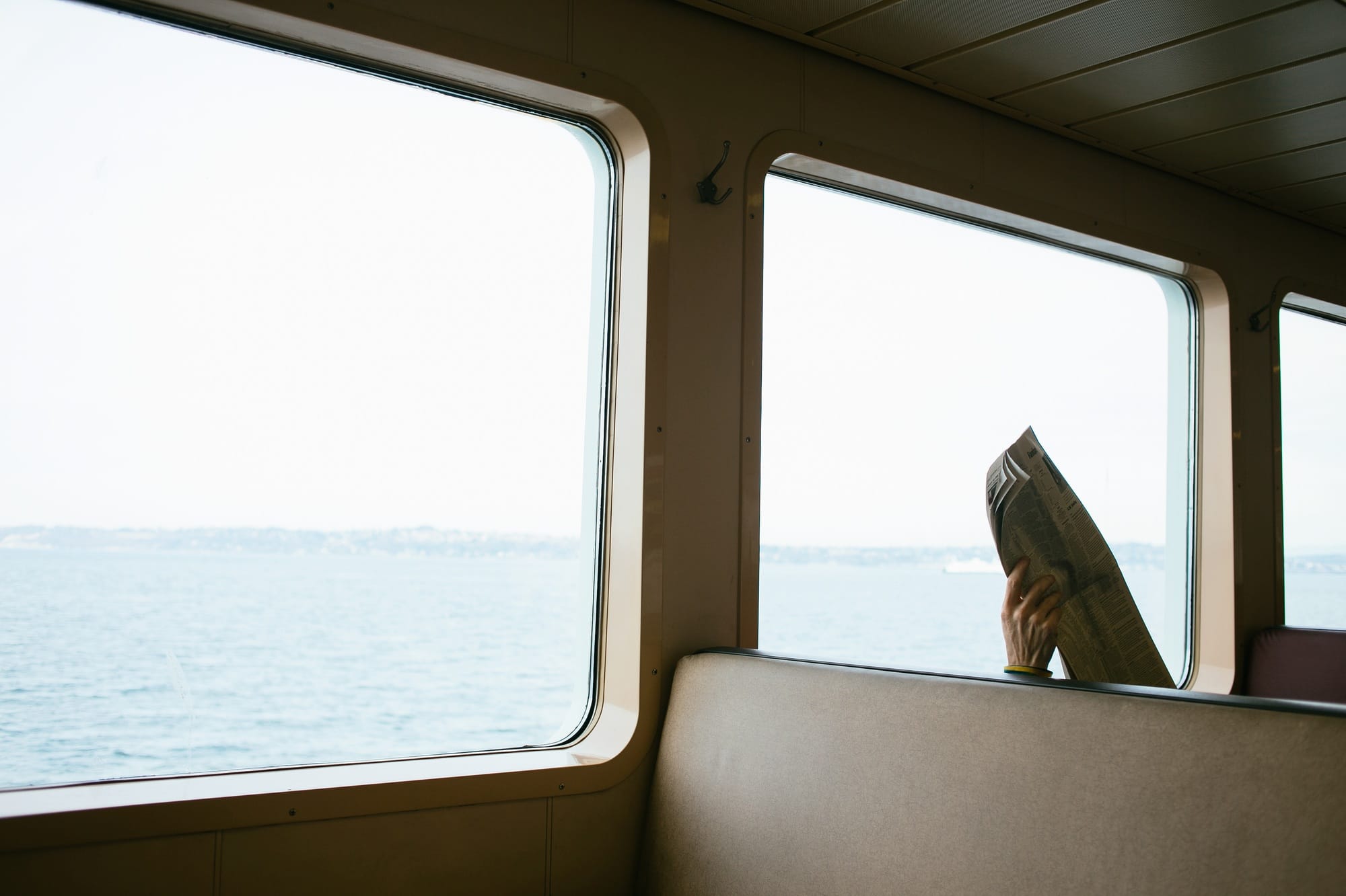 Mans hand holding up newspaper on seat on passenger ferry