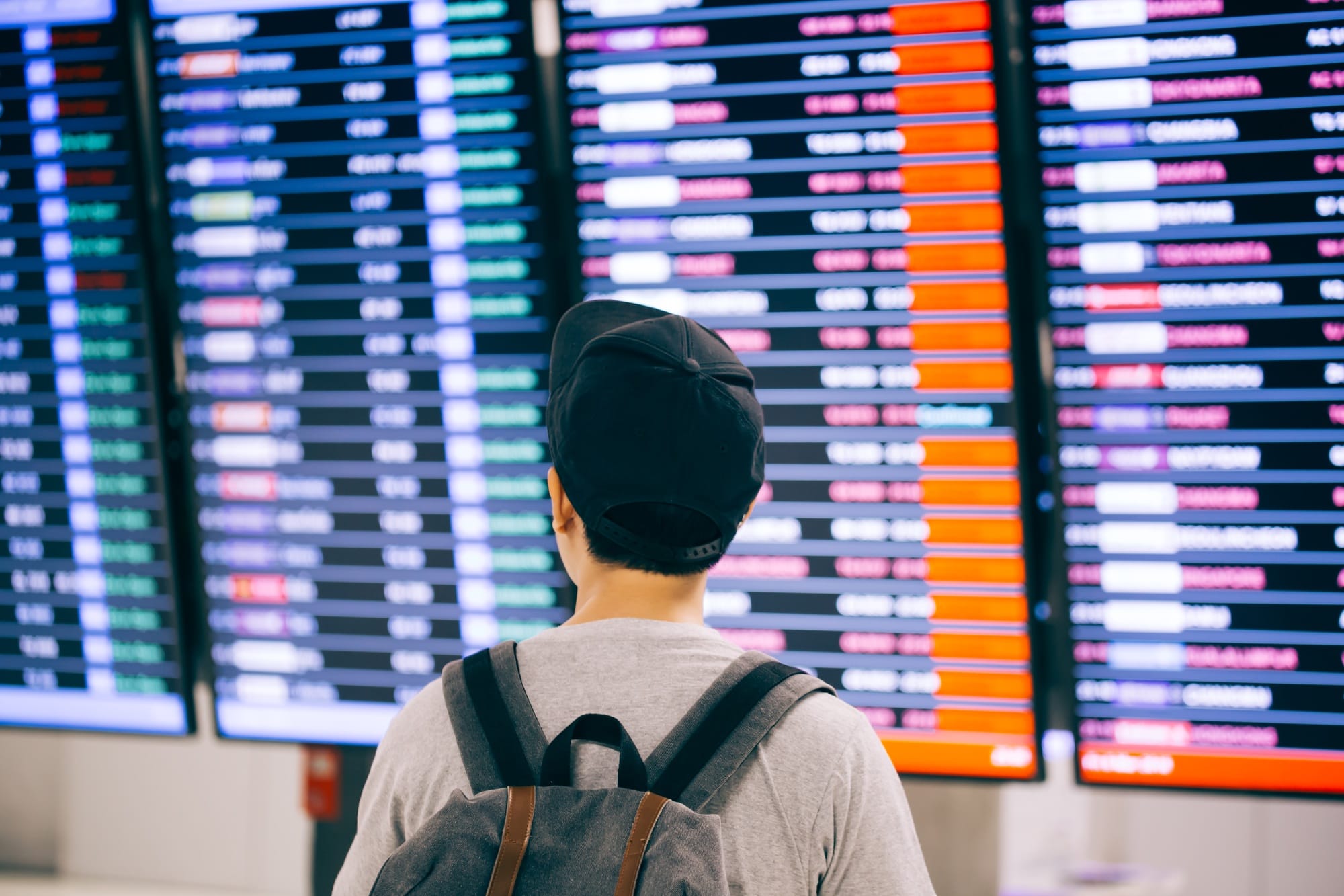 Young male traveler watching and waiting for flight time schedule on boarding time monitor screen